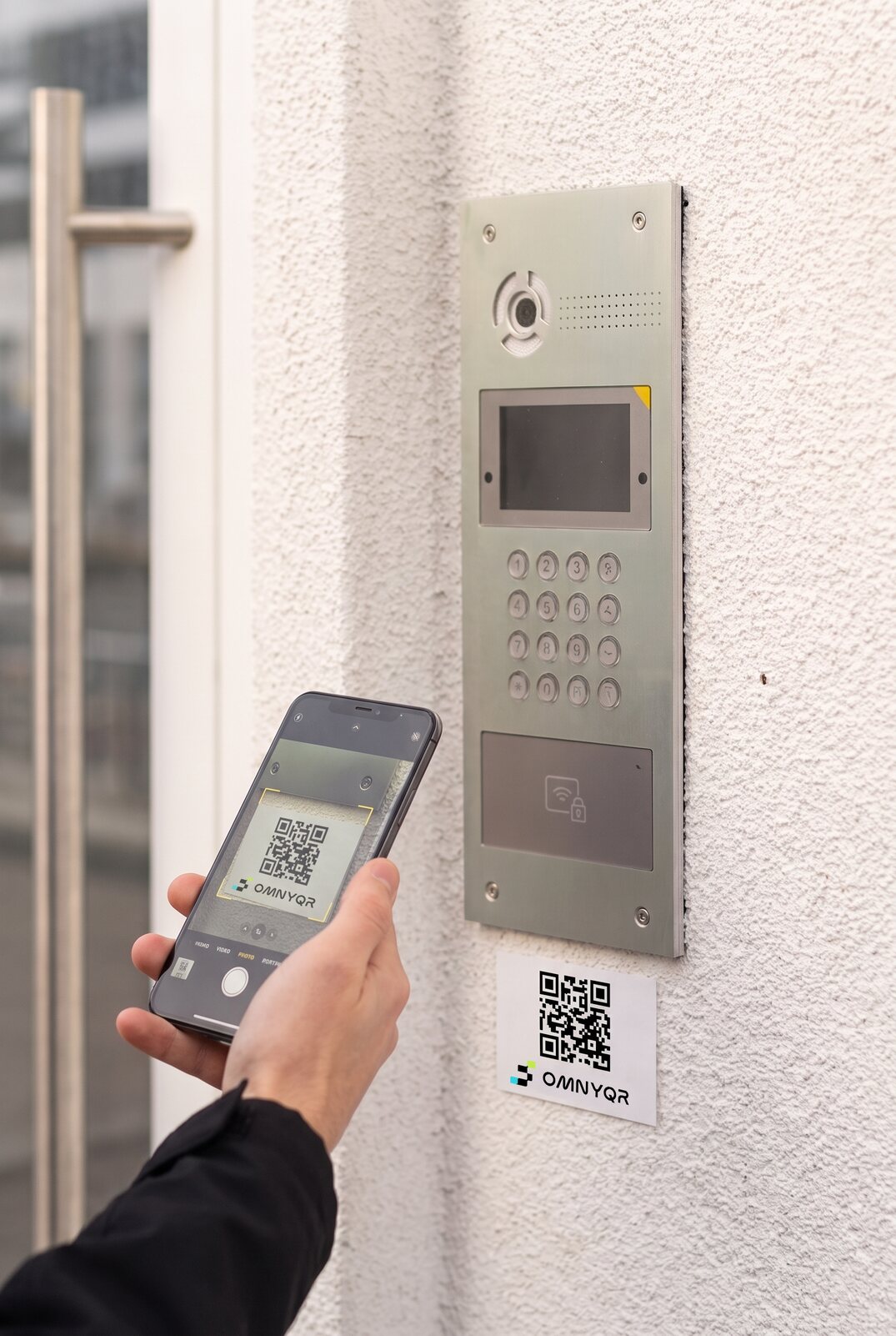Una persona inquadra col telefono il QR OmnyQR applicato su un citofono