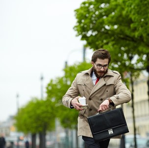 Un uomo in strada controlla l'orologio con la borsa in mano