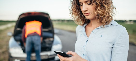 Una donna chiede assistenza dallo smartphone accanto all'auto in panne