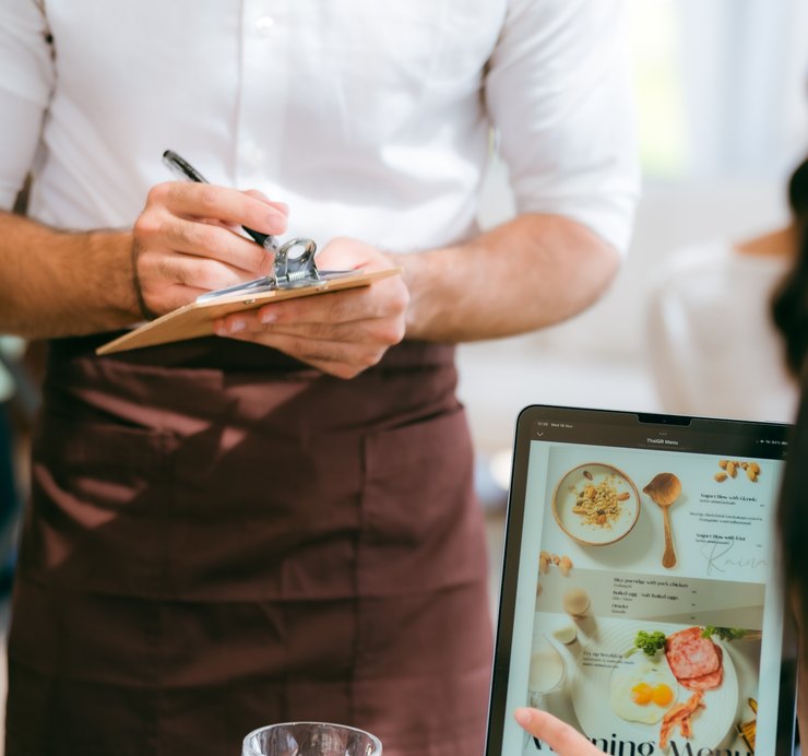 Un cameriere prende un'ordinazione mentre un cliente consulta il menù digitale